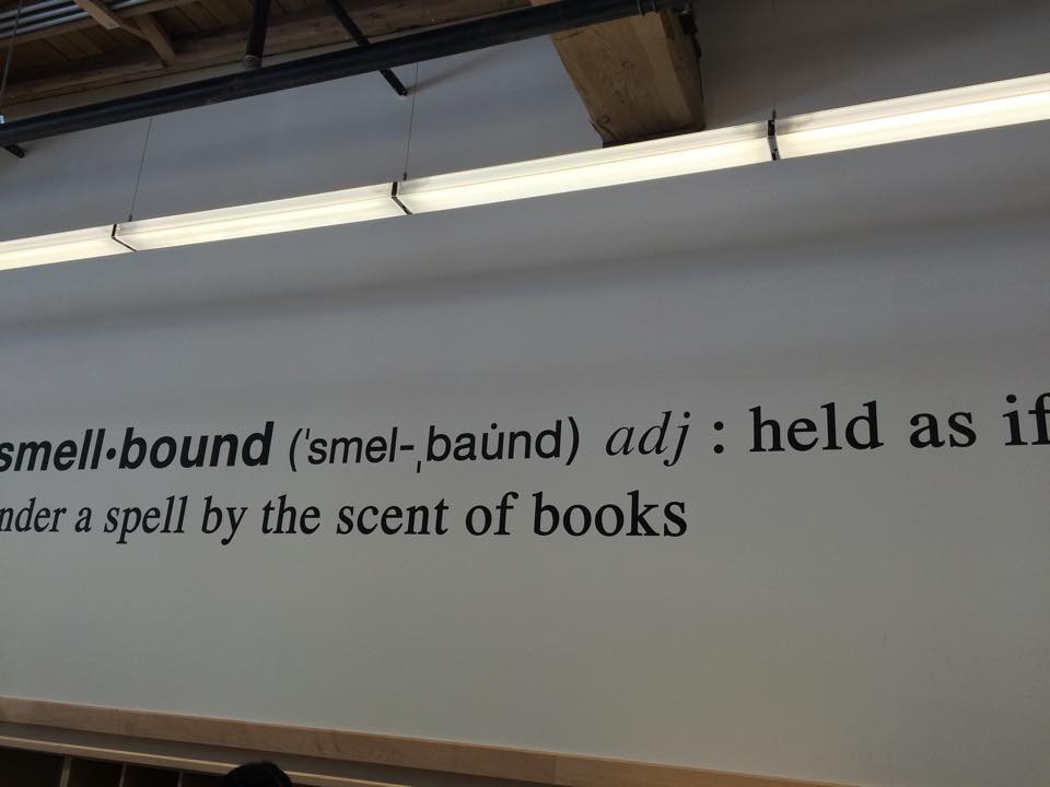 Photo of a wall with the words "smellboud adj: held as if under a spell by the scent of books"