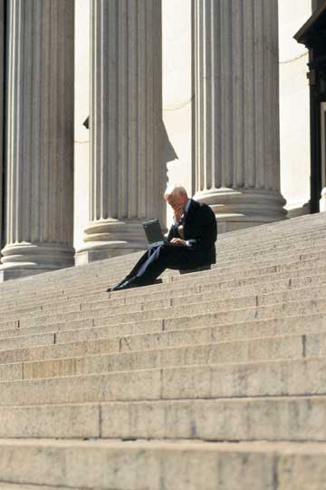 Mature male on laptop on imposing steps with columns in background