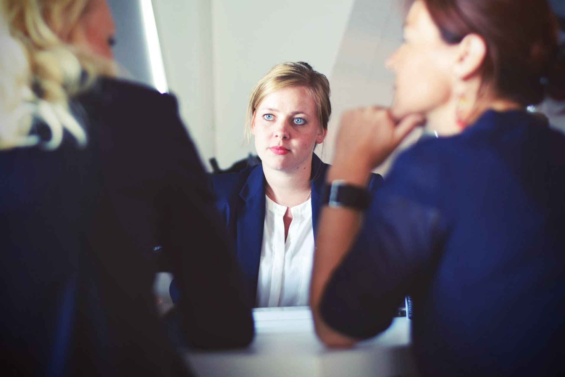 Female student listening as we see the back of two adults sitting at a table facing the student and discussing something.