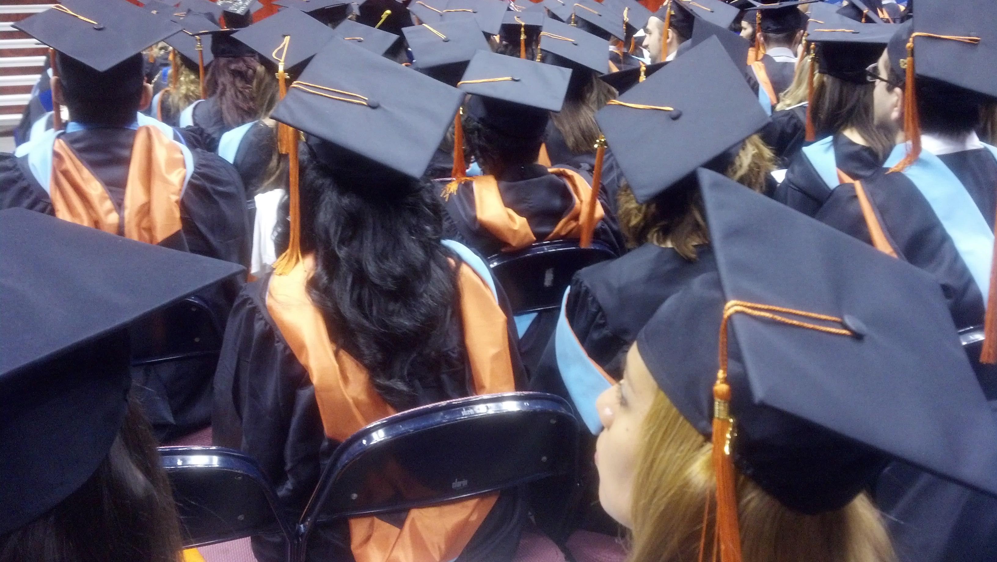 students at graduation sit attentively with their tassles still on the left side of their mortar boards.