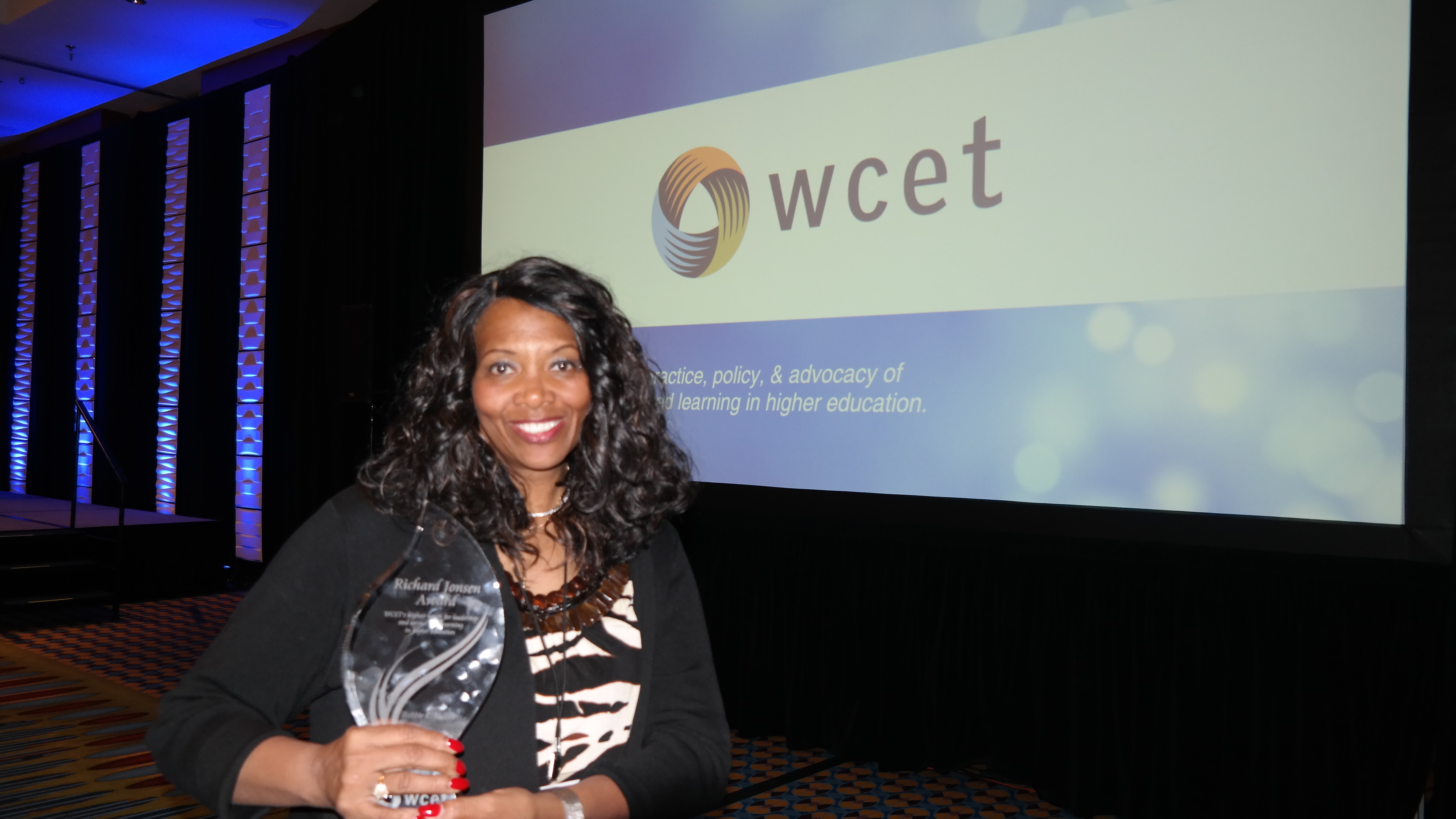 Robbie Melton holding the Richard Jonsen Award in front of a WCET banner