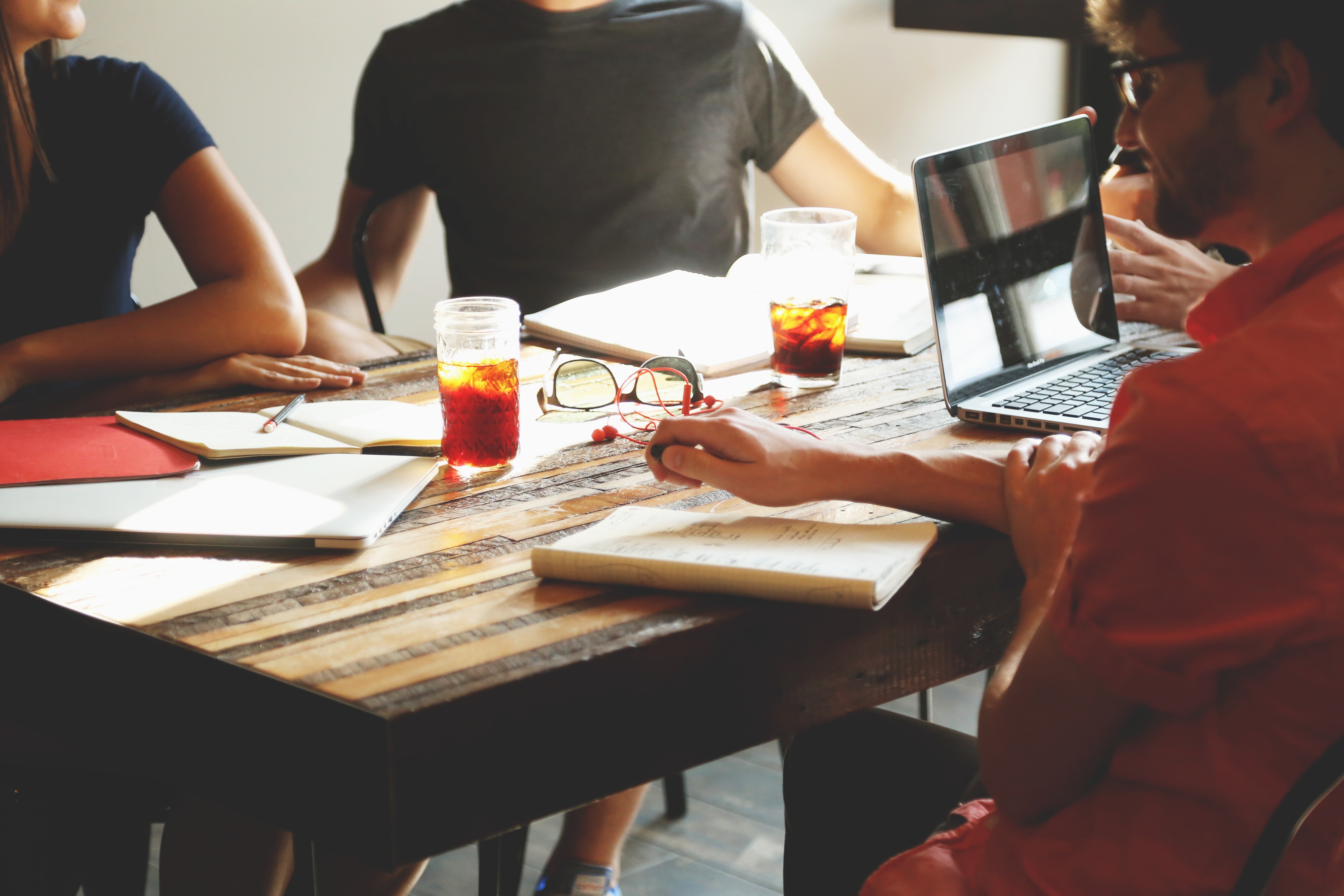 Four people sitting around a table with notebooks and one with a laptop