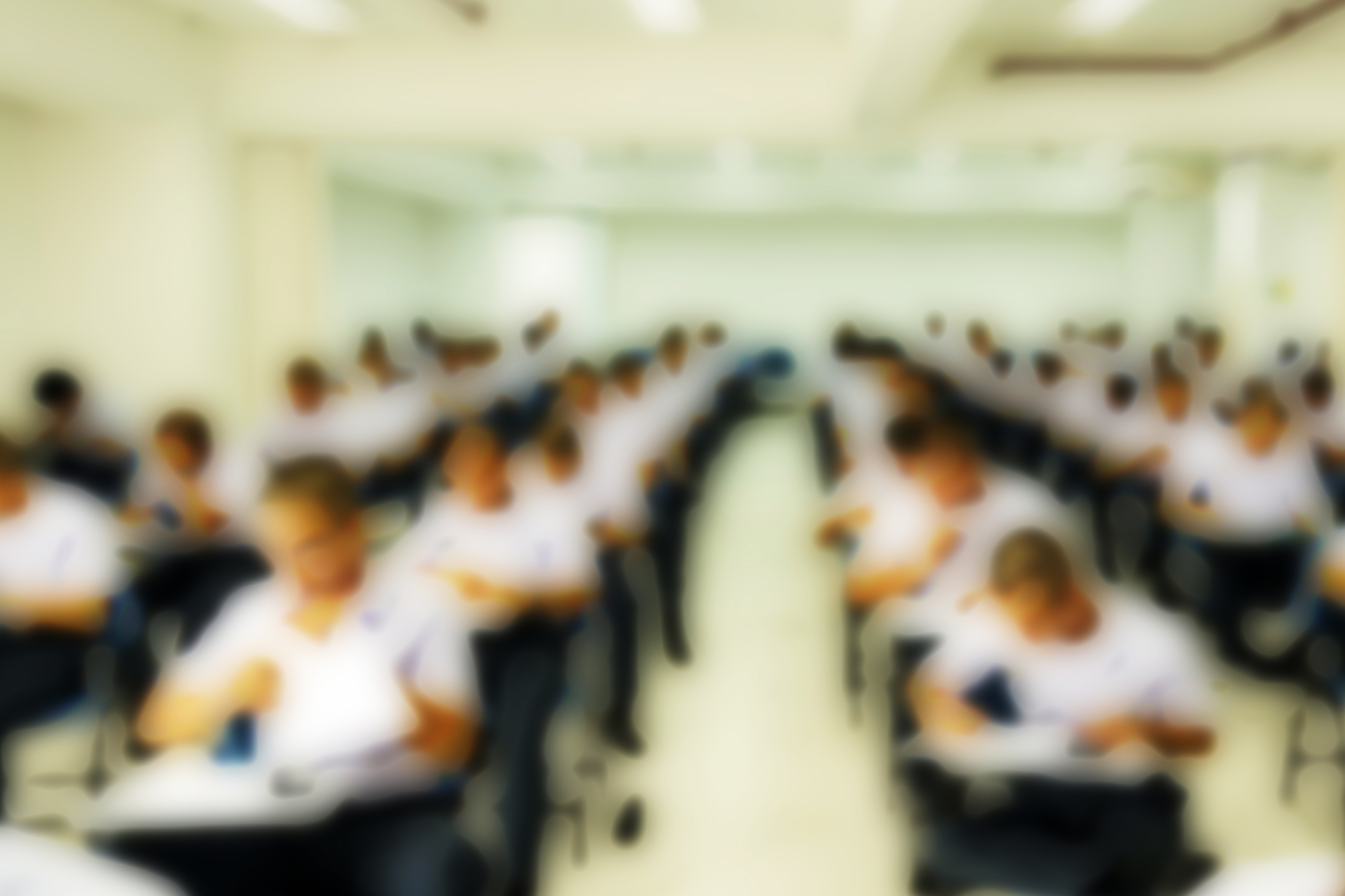 Slight blurry photo of long lines of students sitting in desks studying or taking a test.