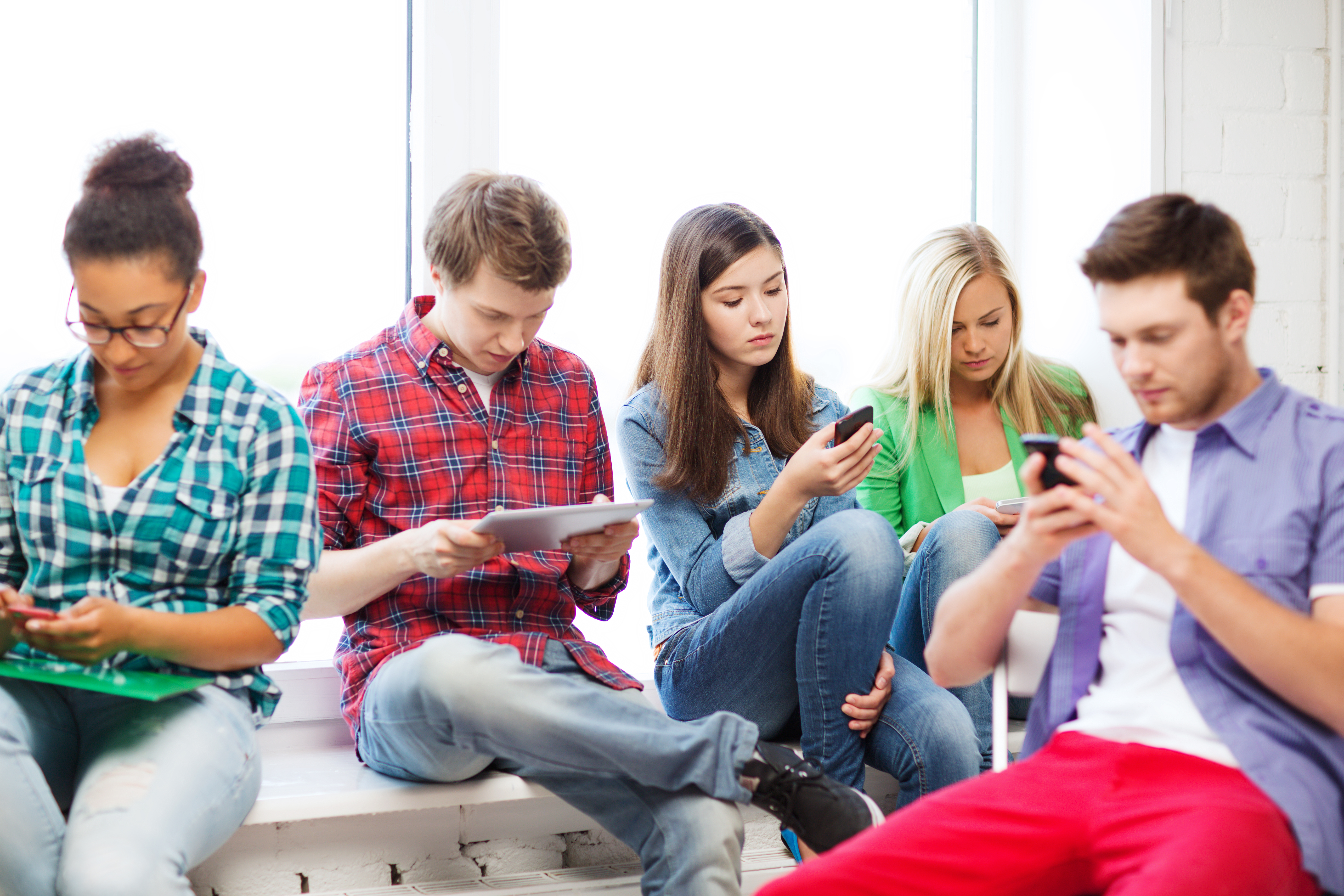 College students sitting in a lose circle, all on a tablet or phone device.