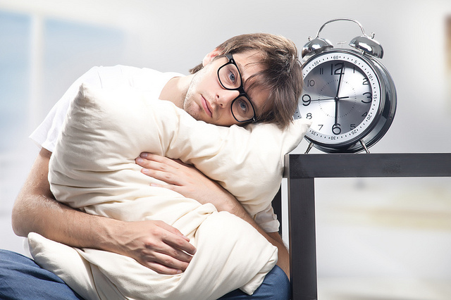 Tired man holding a pillow next to a clock