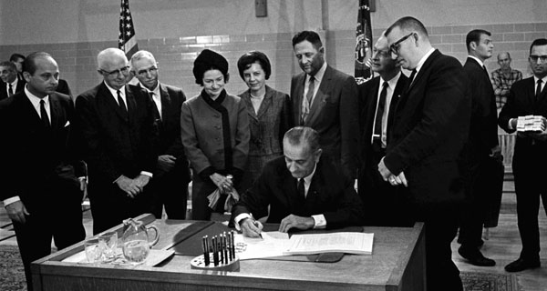 President Lyndon Johnson signing the Higher Ed act surrounded by several witnesses.