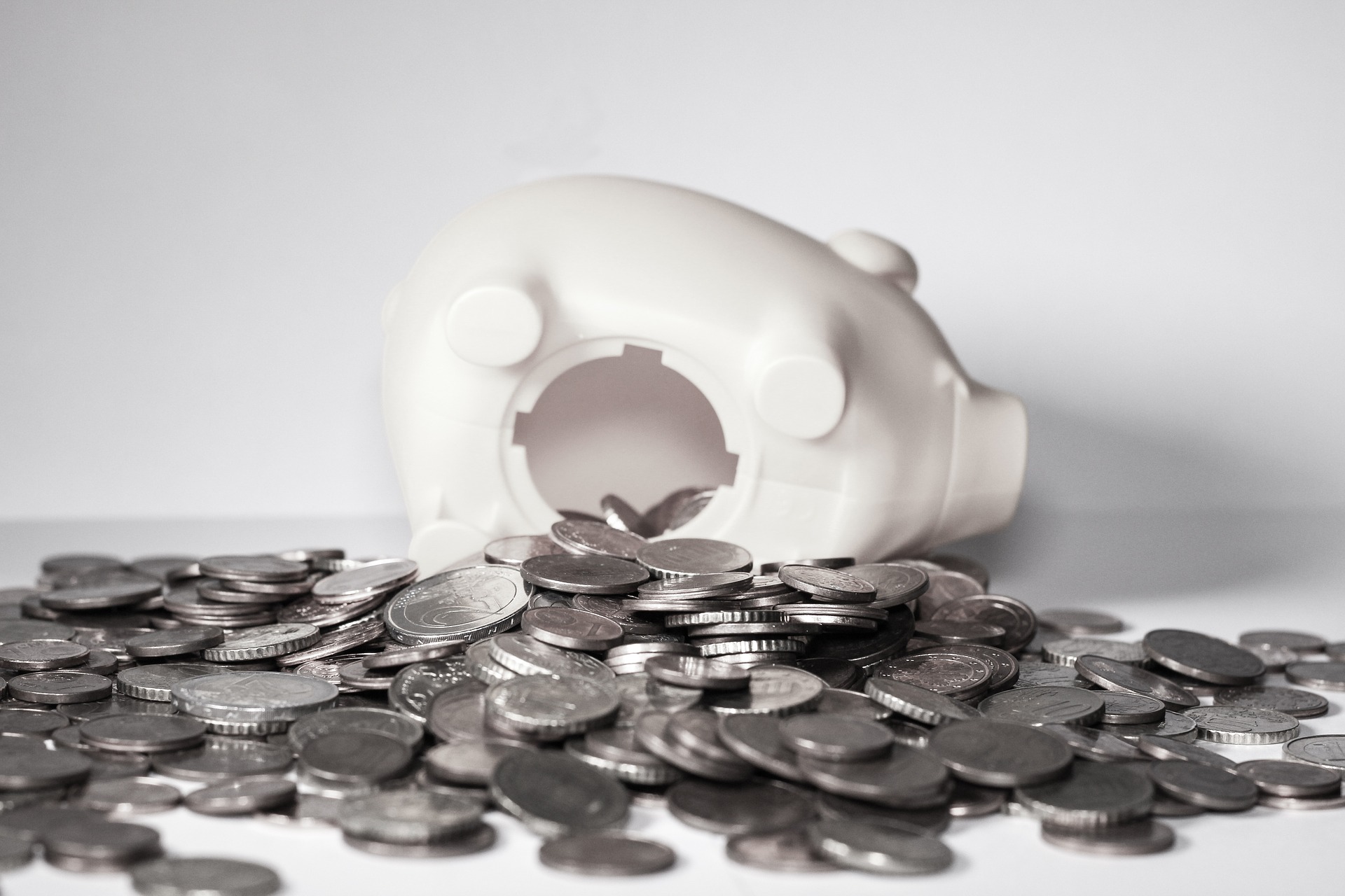 Image of a white piggy bank with the bottom open and coins spilling out