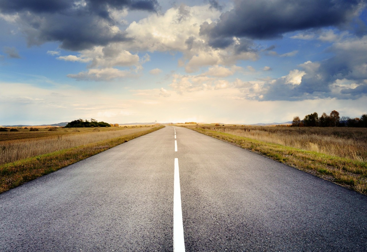 A long, straight road with blue sky and clouds.