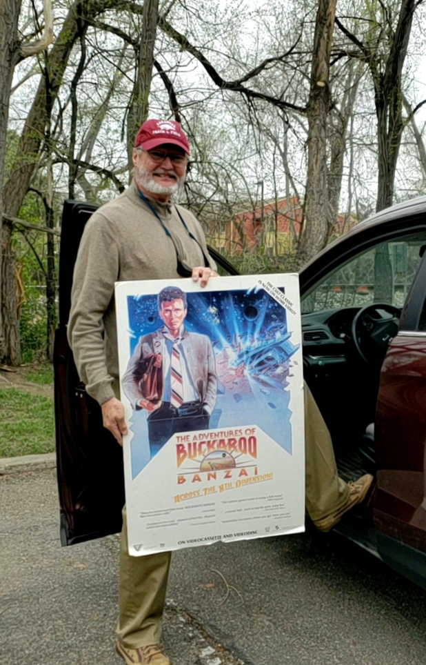 Mike standing outside his carholding a Buckaroo Banzai movie poster