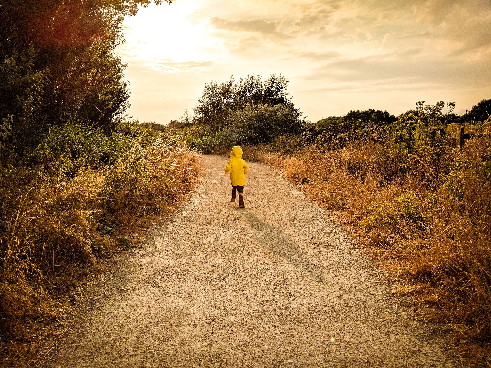 A child in a yellow raincoat runs down a road