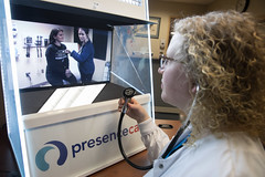Picture of a nurse looking at a computer screen that shows another nurse and a patient.