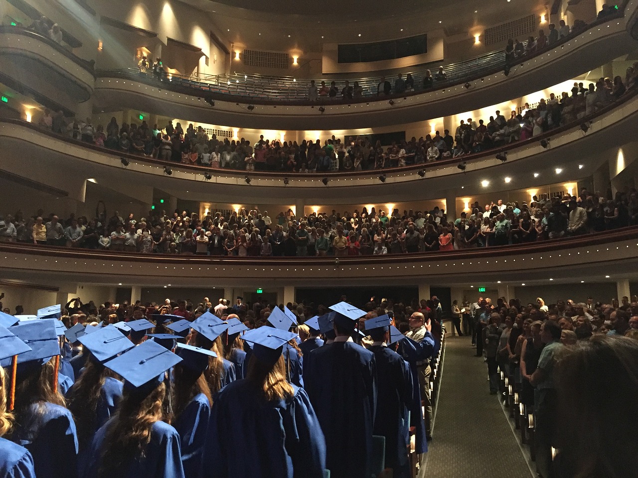 A large auditoriam filled with people looking over groups of college graduates in graduation regalia