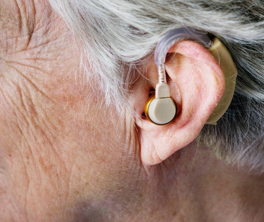 Photograph of the side of a person’s head and a hearing aid attached to their ear.