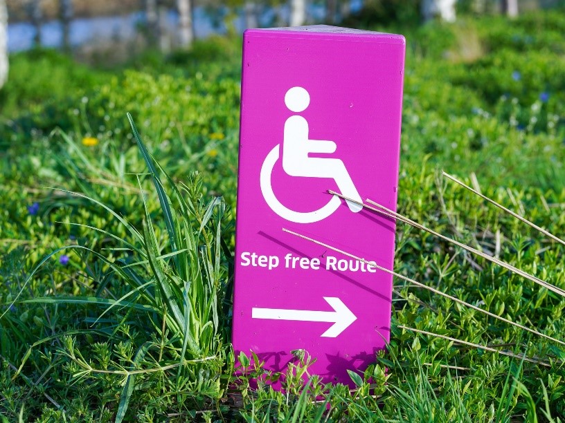 Photograph showing a pink accessibility sign, which points towards a “Step Free Route.”