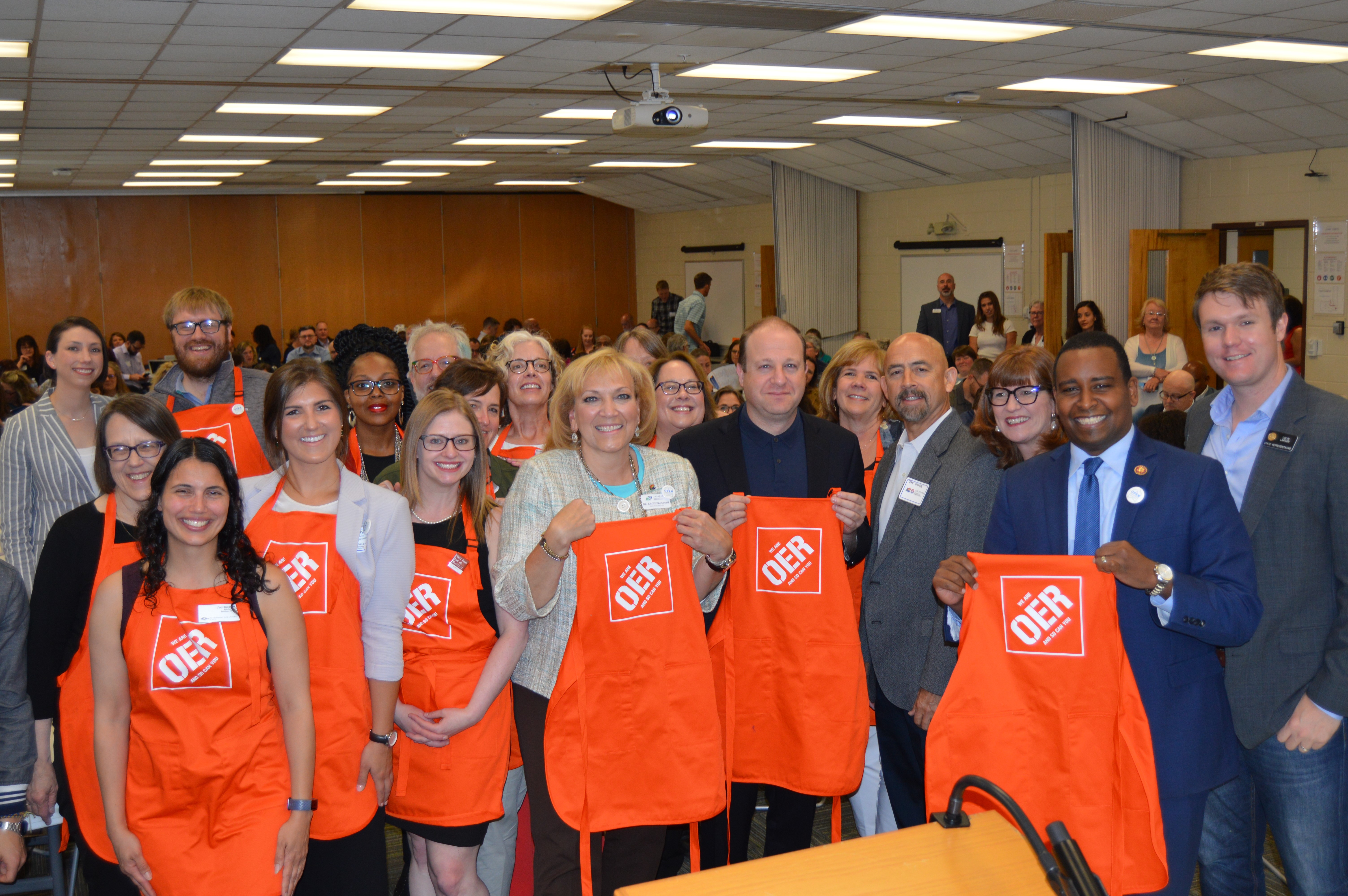 Attendees at a conference pose for a photo holding aprons that read "OER"