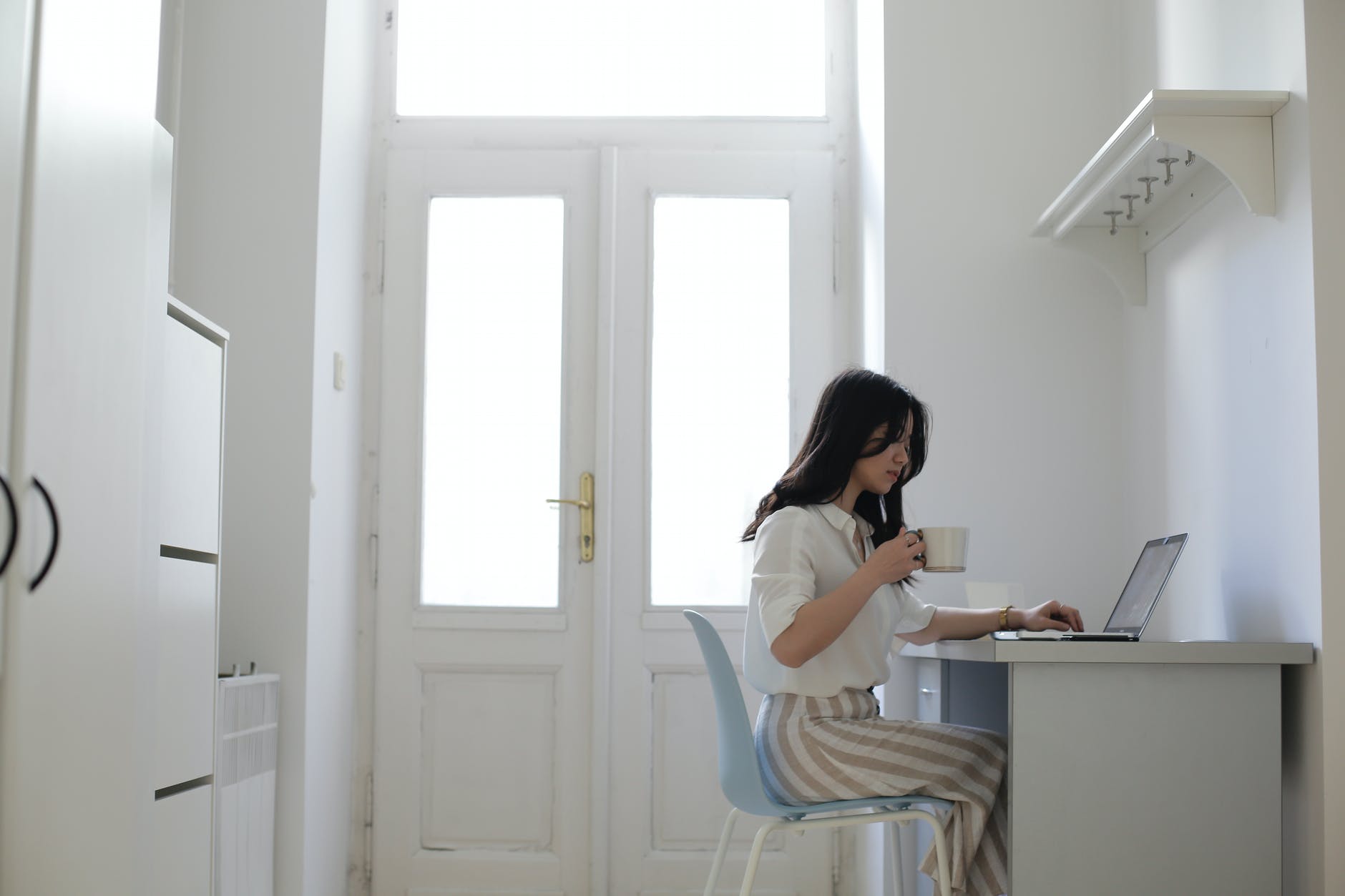 woman working from remotely at a small desk with a cup of coffee in hand. 