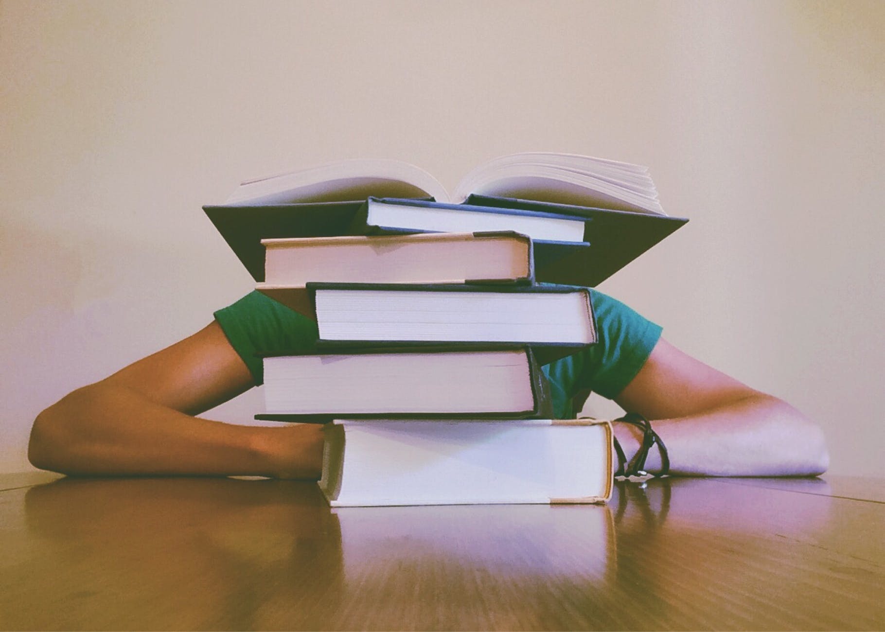 a student with their head down behind a stack of books