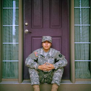young person in a military uniform sitting in front the entrance to a home
