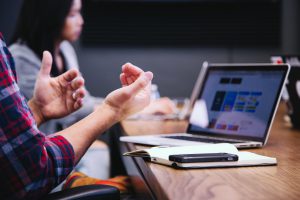 Person in plaid shirt gesturing at a laptop