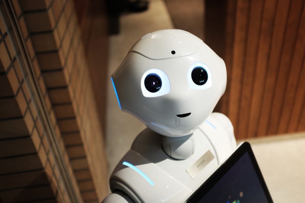Image of a robot assistant white big eyes carrying a computer. 