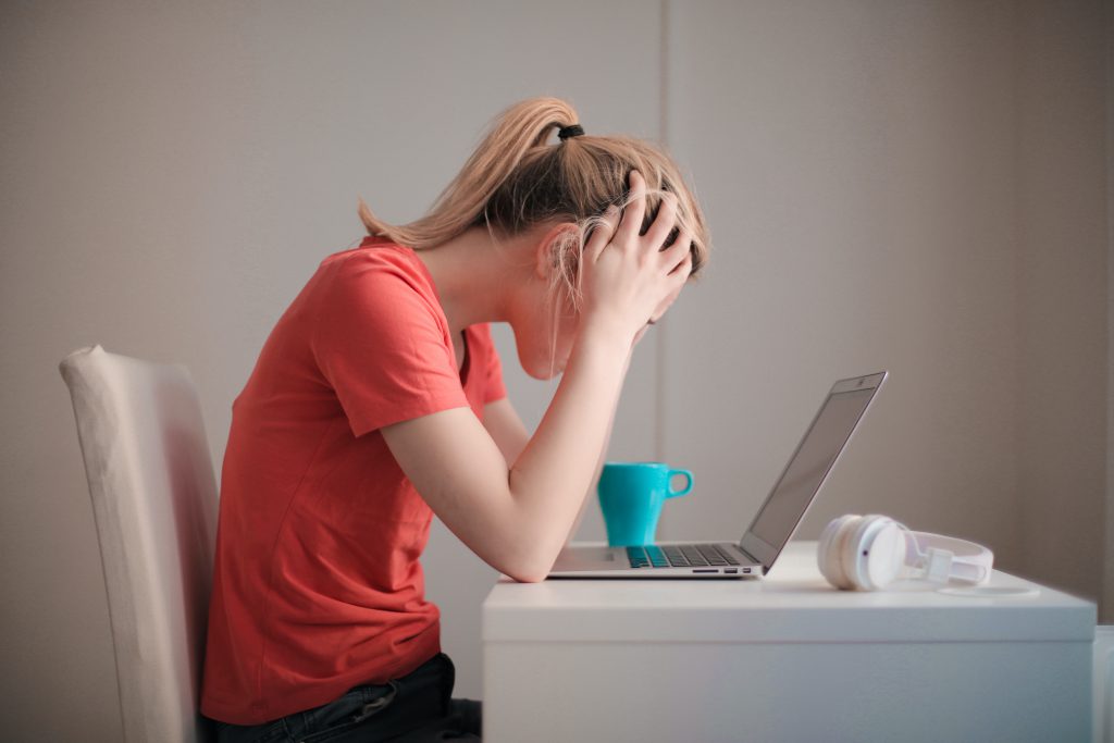a young woman holds her hands on her head - indicating frustration - while looking at a laptop