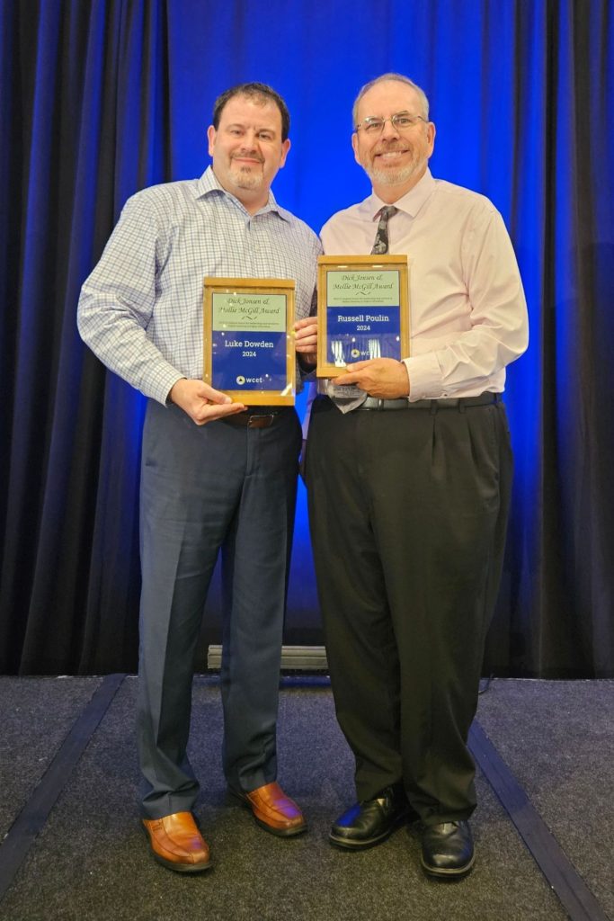 Photo of Luke Dowden and Russ Poulin holding award plaques in front of a blue curtain.