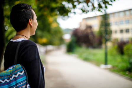 Traditional college aged student smiling and looking at a campus building
