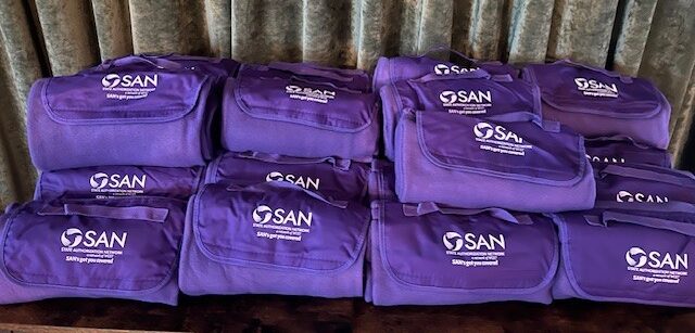 A table stacked with purple blankets with the SAN logo