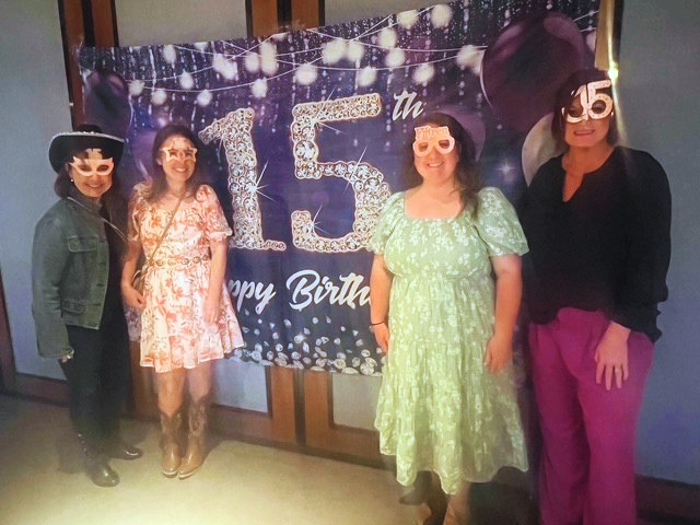 SAN Staff wearing festive sunglasses in front of a 15th anniversary banner