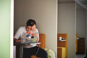 Photo of male college student sitting at a table with laptop open, with and anxious look on his face