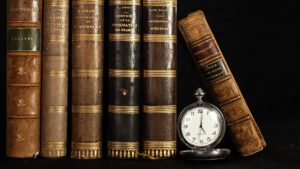 Old leather bound books on a shelf next to a pocketwatch