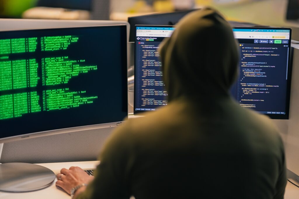 The back of a man wearing a hoodie facing two computer screens of code
