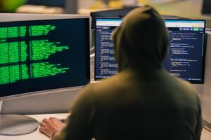 The back of a man wearing a hoodie facing two computer screens of code
