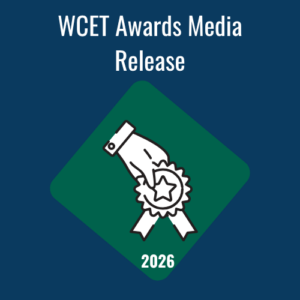 A digital graphic featuring a dark blue background with the text "WCET Awards Media Release" in bold white letters at the top. In the center, there is a green diamond shape containing a white line-art icon of a hand holding a star-shaped award ribbon. The year "2026" is written in white at the bottom point of the diamond.