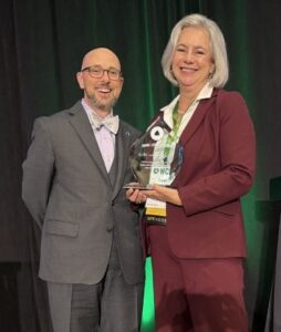 Leah Matthews holds the glass WCET Jonsen and McGill Award on stage beside WCET Executive Director Van Davis.